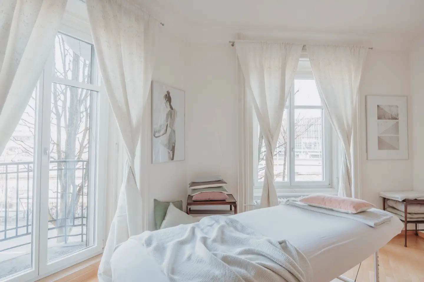 Behandlungsraum für Craniosacral Therapie in der Praxis Zentral an der Zentralstrasse 38 in Luzern: Massageliege mit weisser Decke vor hohen Altbaufenstern mit hellen Vorhängen.